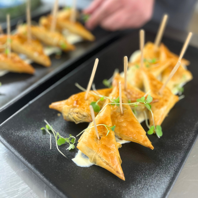 Plate of 9 triangular spanakopitas in a garlic aioli with toothpicks