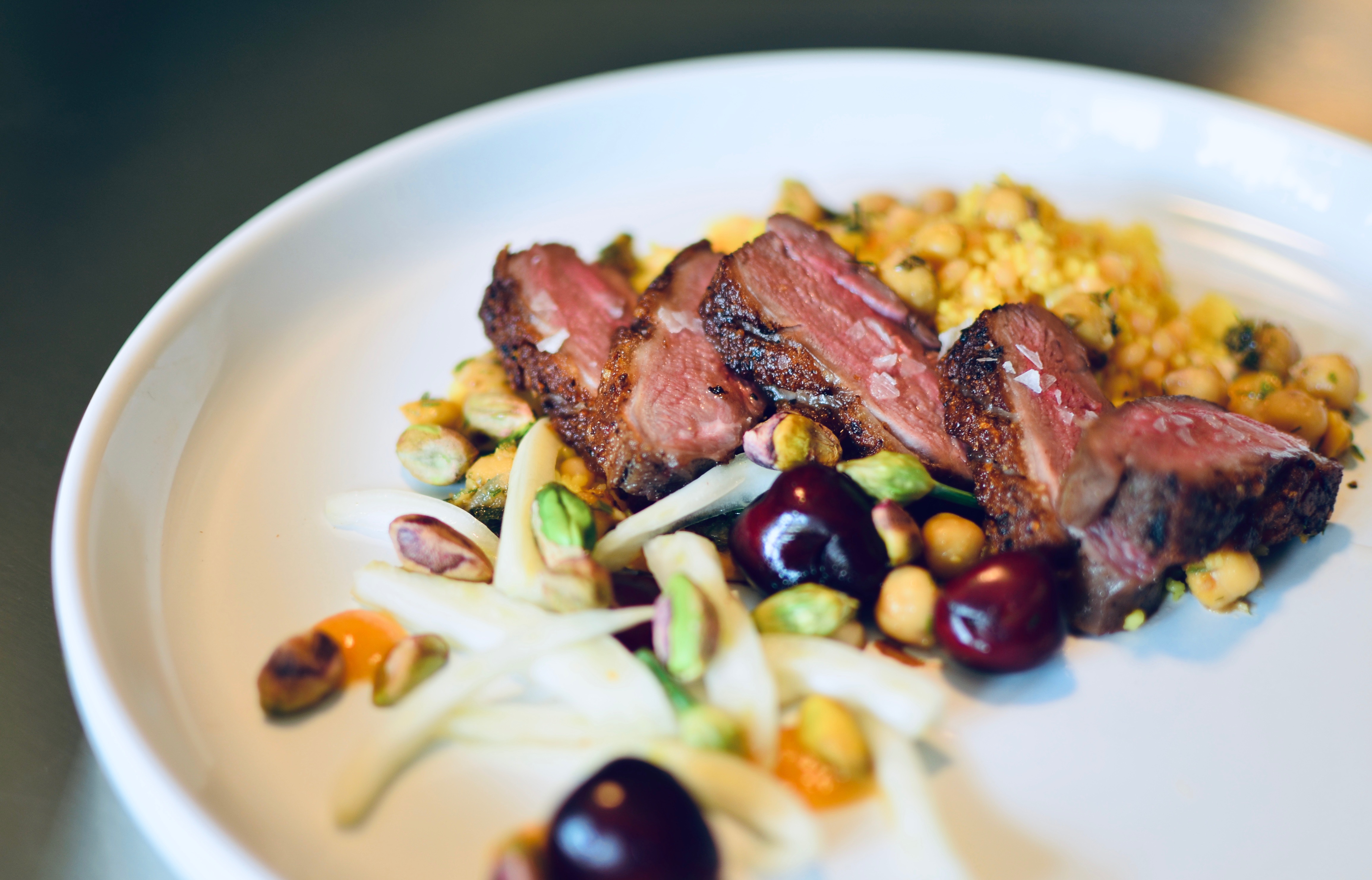 Plate of duck confit with Morrocan spiced couscous with fennel, cherries, and pistachios.