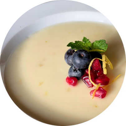 Lemon posset in a white bowl with blueberries, pomegranate seeds, mint, and lemon zest
