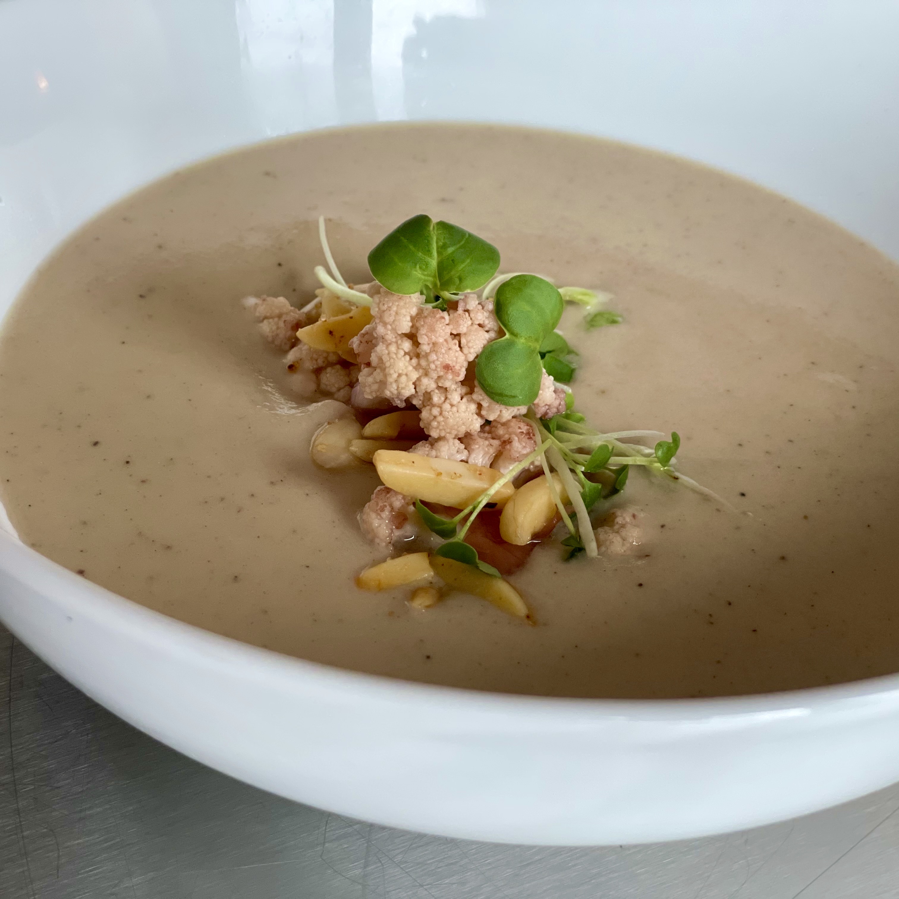 Bowl of Curried Coconut Cauliflower Soup with Pickled Cauliflower, Shaved Almonds, and Microgreens.