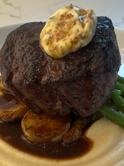 Beef tenderloin on roasted potatoes, French beans, and celeriac puree, topped with lemon-herb compound butter