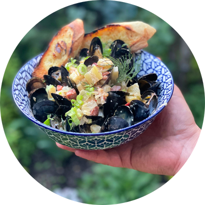 Hand holding a blue and white bowl with mussels in white wine-shallot broth with green onions