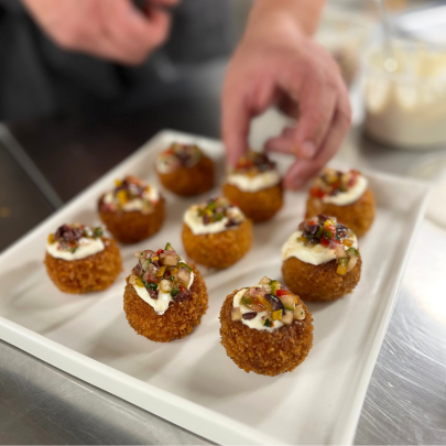Plate of 9 roasted red pepper arancini appetizers topped with whipped goat cheese and olive tapenade